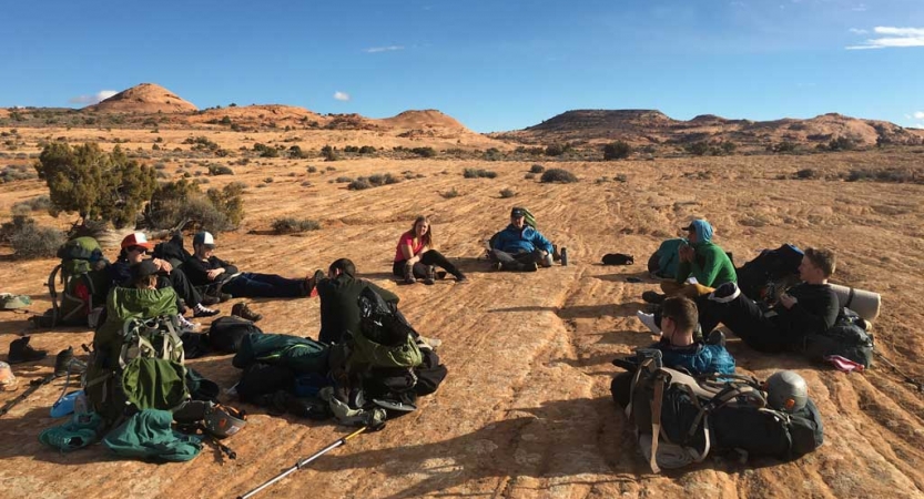 A group of people take a break from backpacking and sit in a desert landscape.